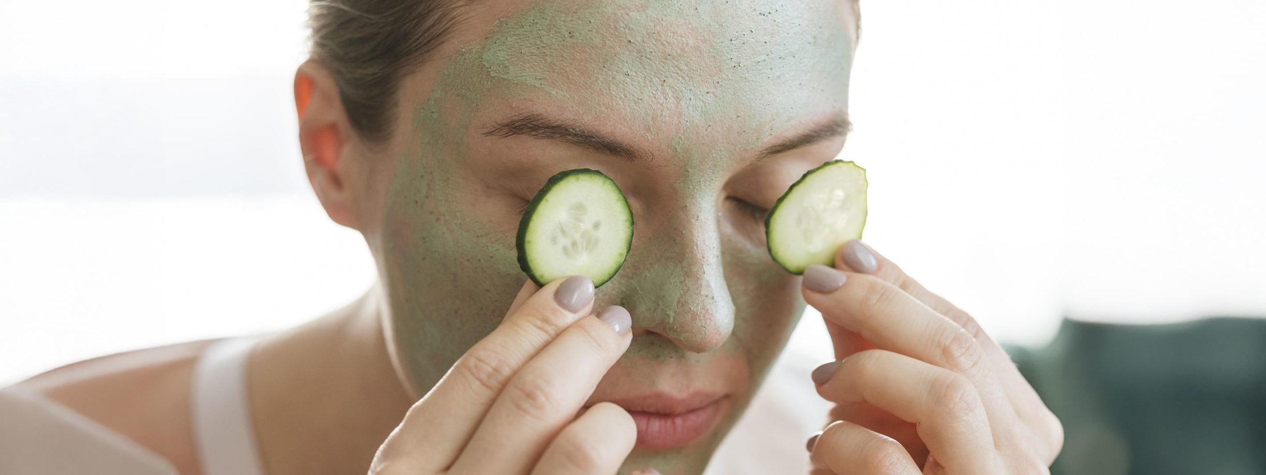 woman with facial mask putting slices cucumber