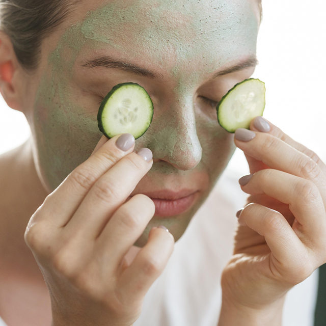 woman with facial mask putting slices cucumber